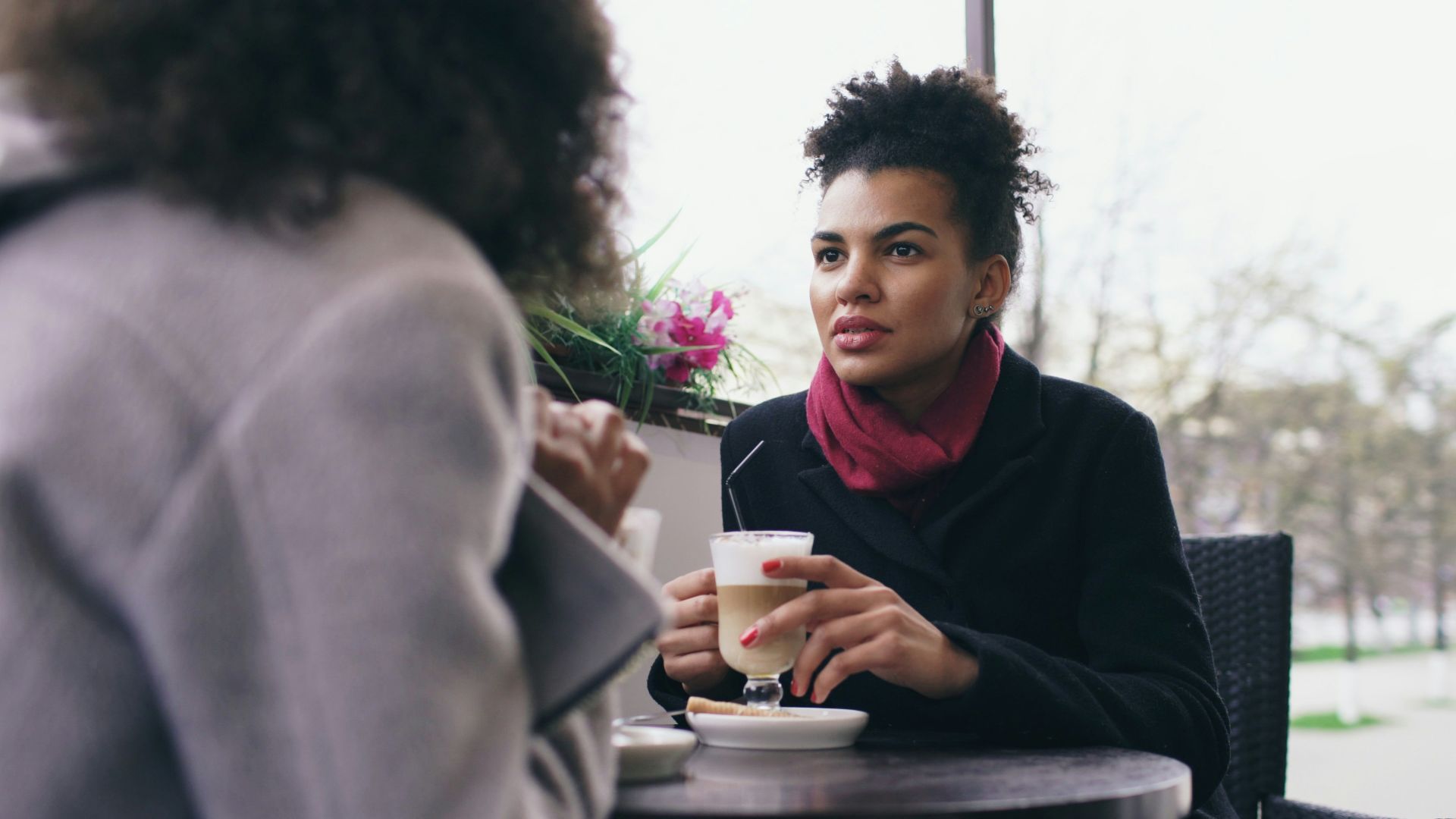 Two women talking at an outdoor cafe table.