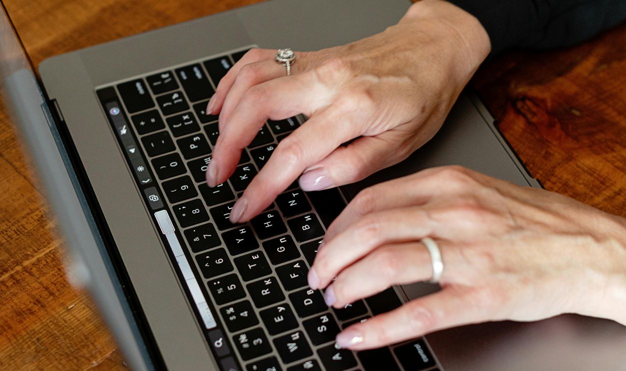 Person Using Macbook Pro on Brown Wooden Table