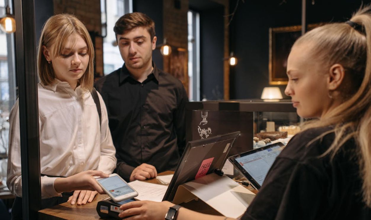 A Woman in White Long Sleeves Tapping Her Phone on a Payment Terminal at the Counter