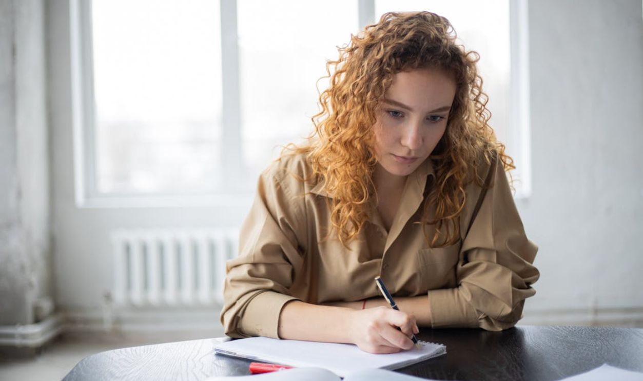 Pensive female student writing notes while studying in light room