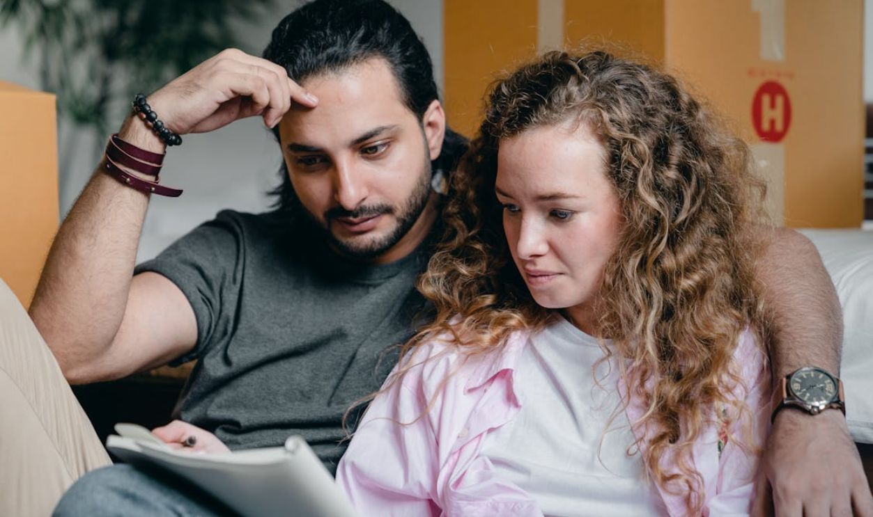 Pensive couple looking through notebook while sitting near boxes
