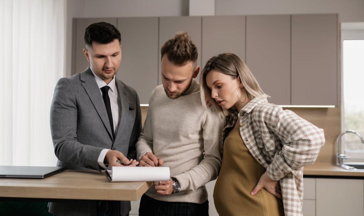 Man in Gray Jacket Showing Documents to a Man and Pregnant Woman