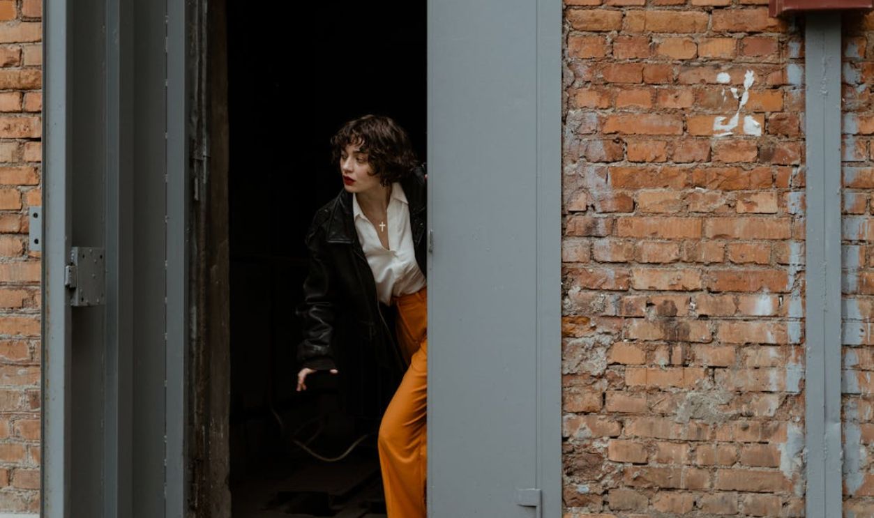 A Woman in Black Jacket Walking Out of a Gray Doorway