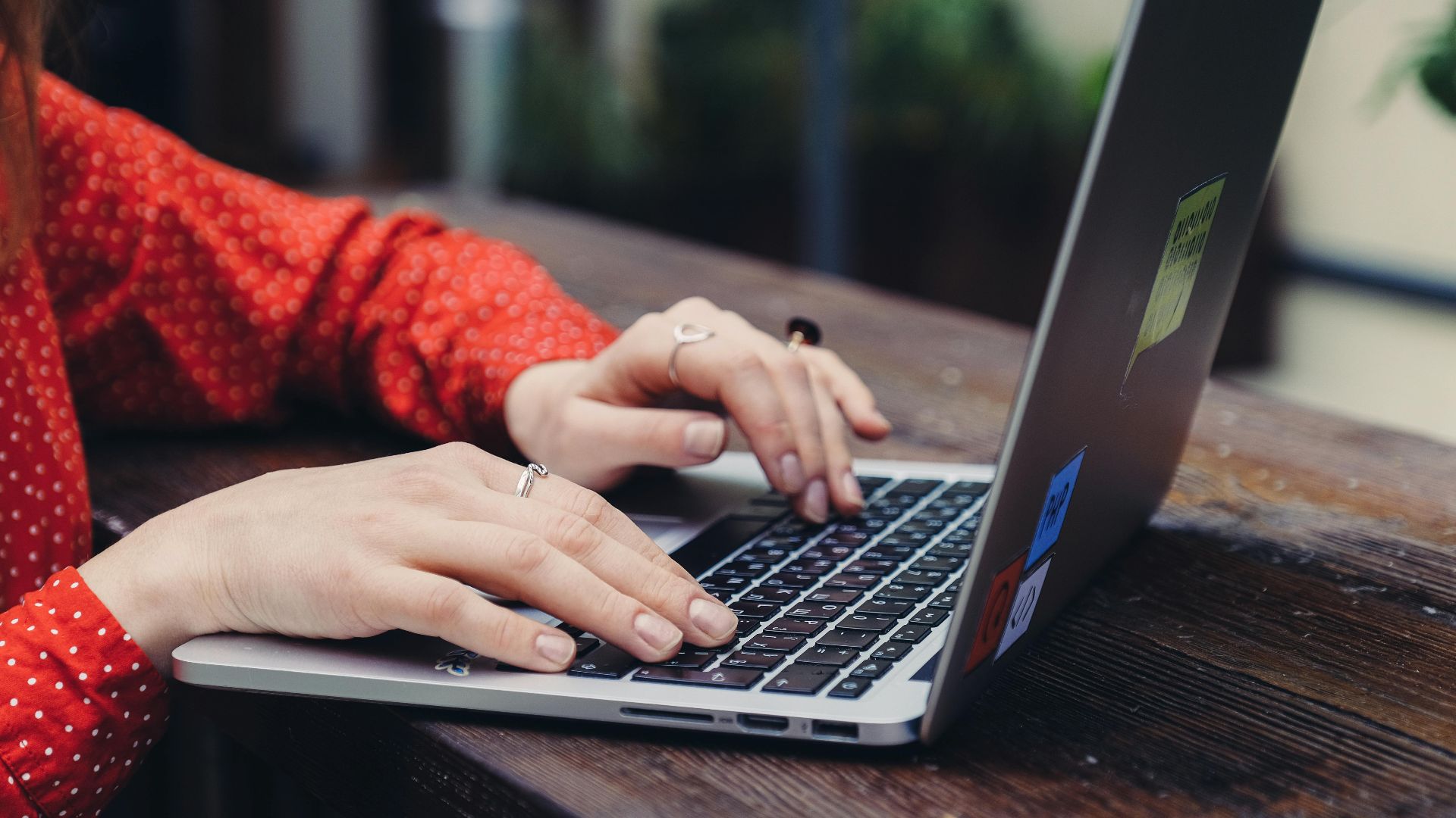 Close-up of hands typing on a laptop placed on a wooden table outdoors.