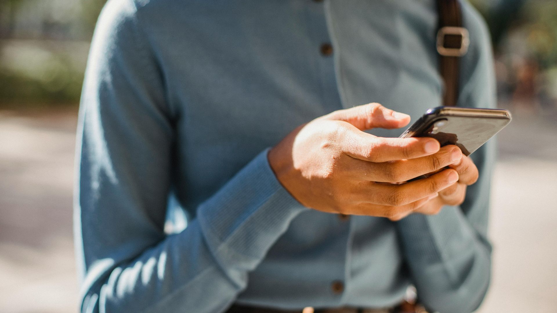 Close-up of a person using a smartphone outdoors, focusing on hands and mobile device.