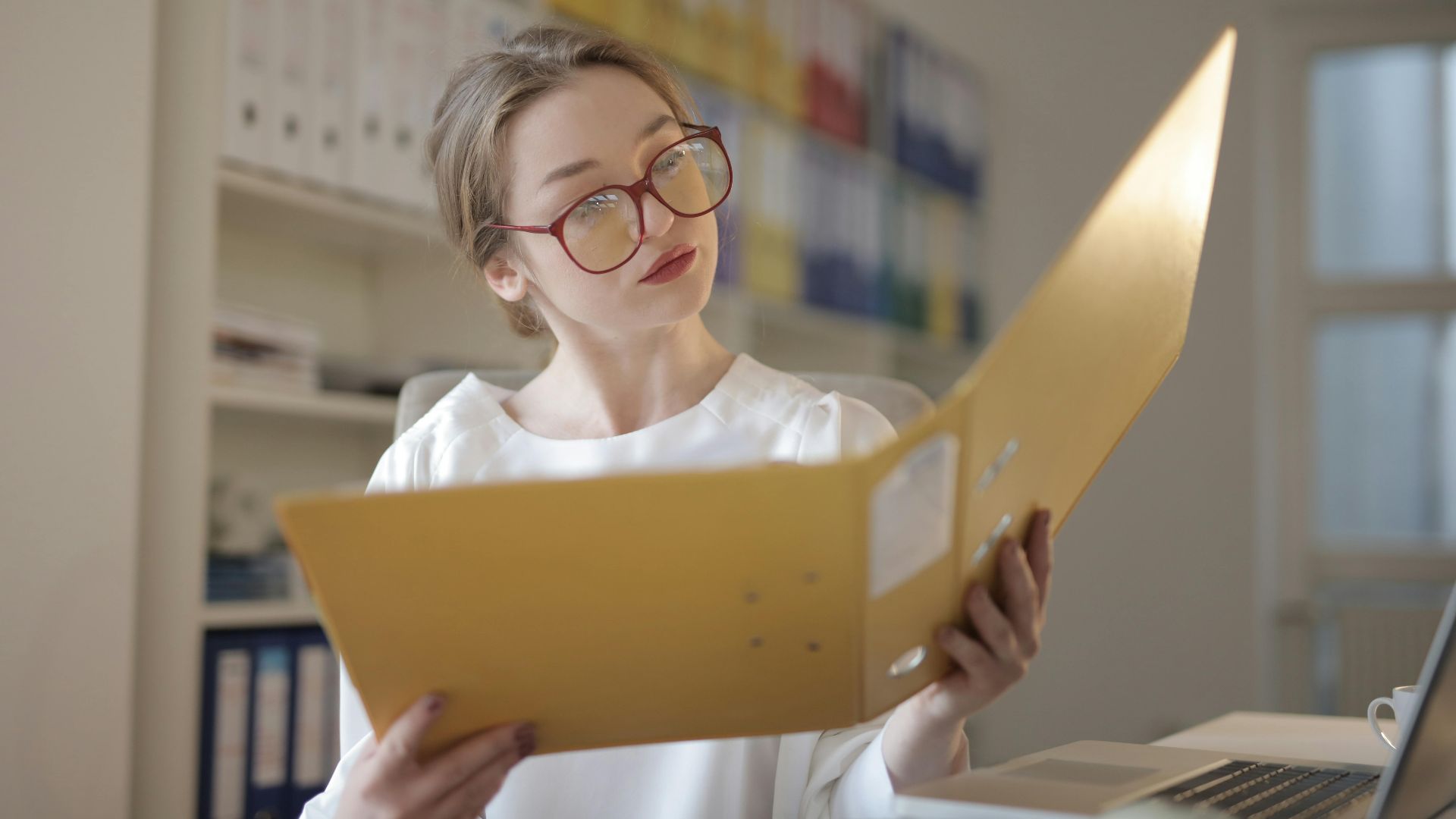 Caucasian woman intensely reading documents in an office setting.