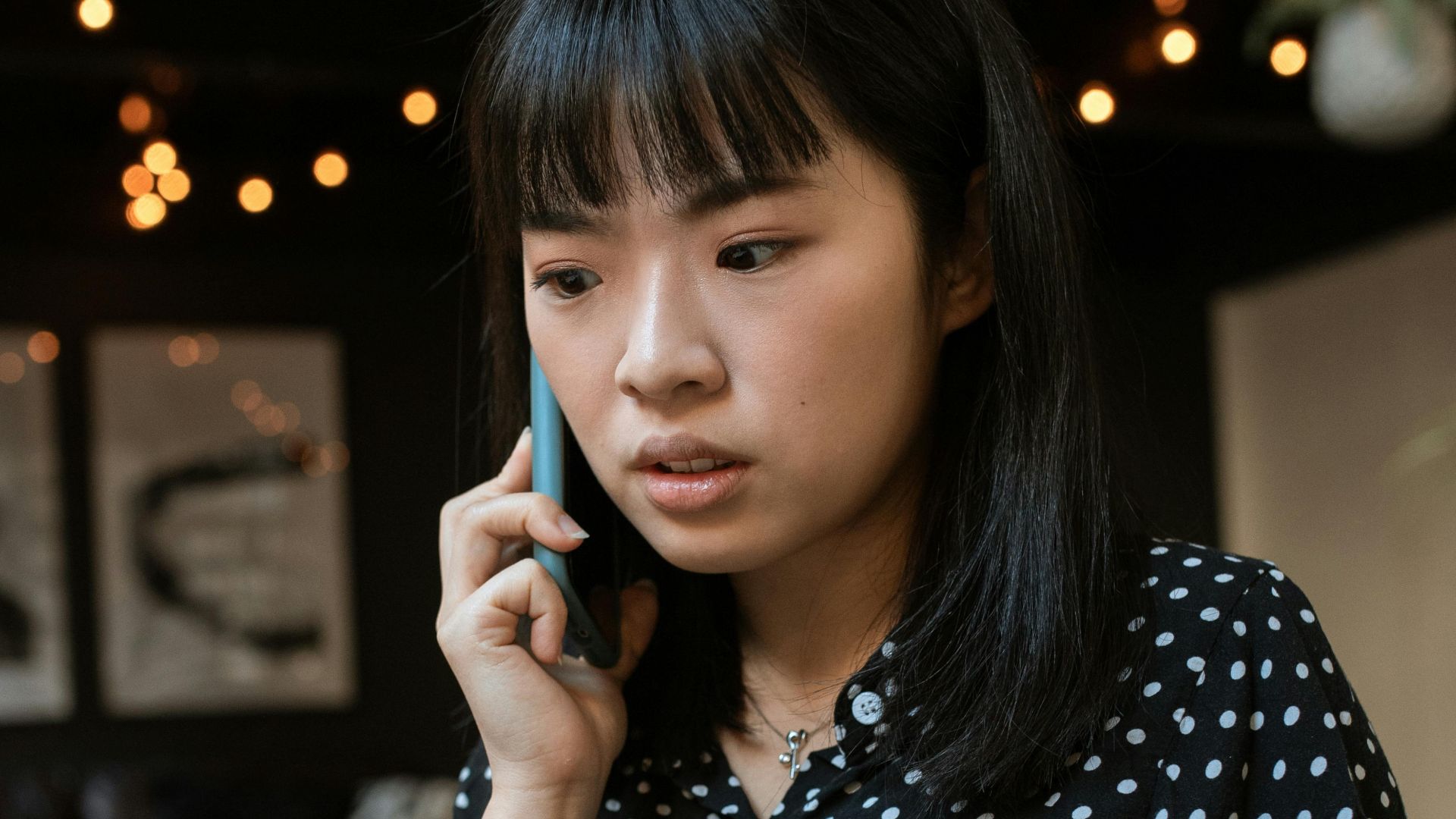 Focused young woman in a polka dot blouse taking a call indoors.