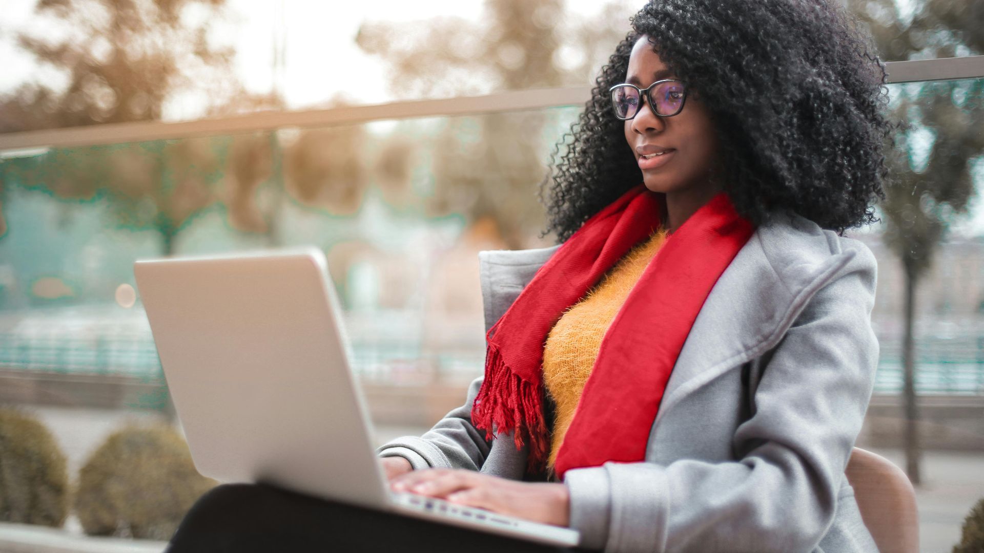 A woman working remotely on a laptop outdoors in a park setting. Stylish and focused.