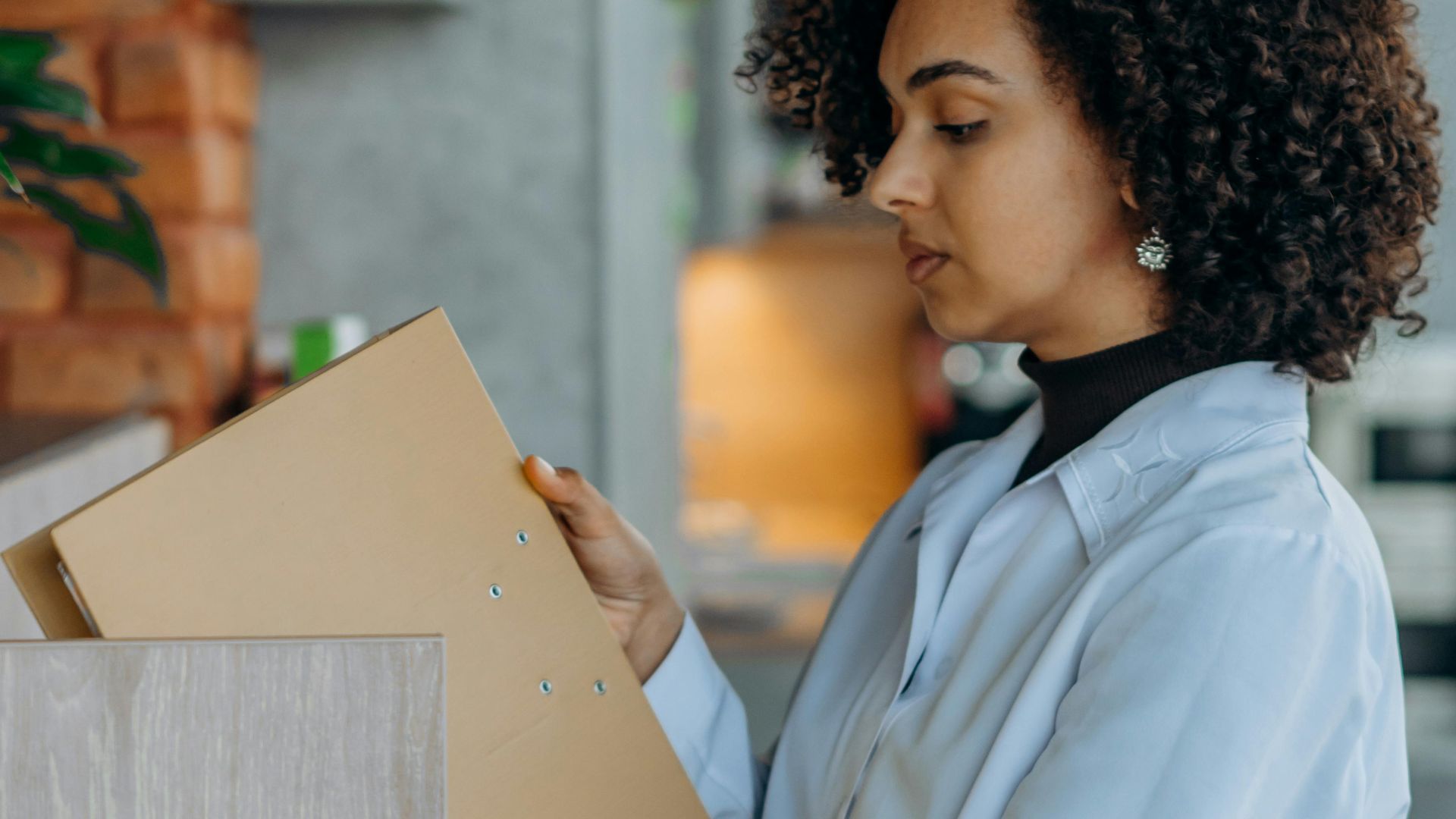 Side view of an adult woman with afro hair organizing files in a modern office.