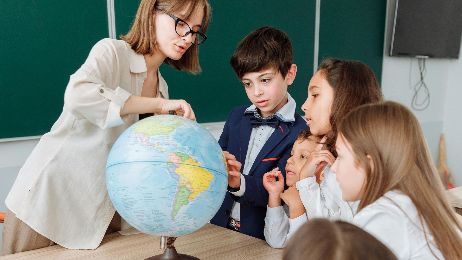 Teacher and students exploring geography with a globe in a classroom setting.