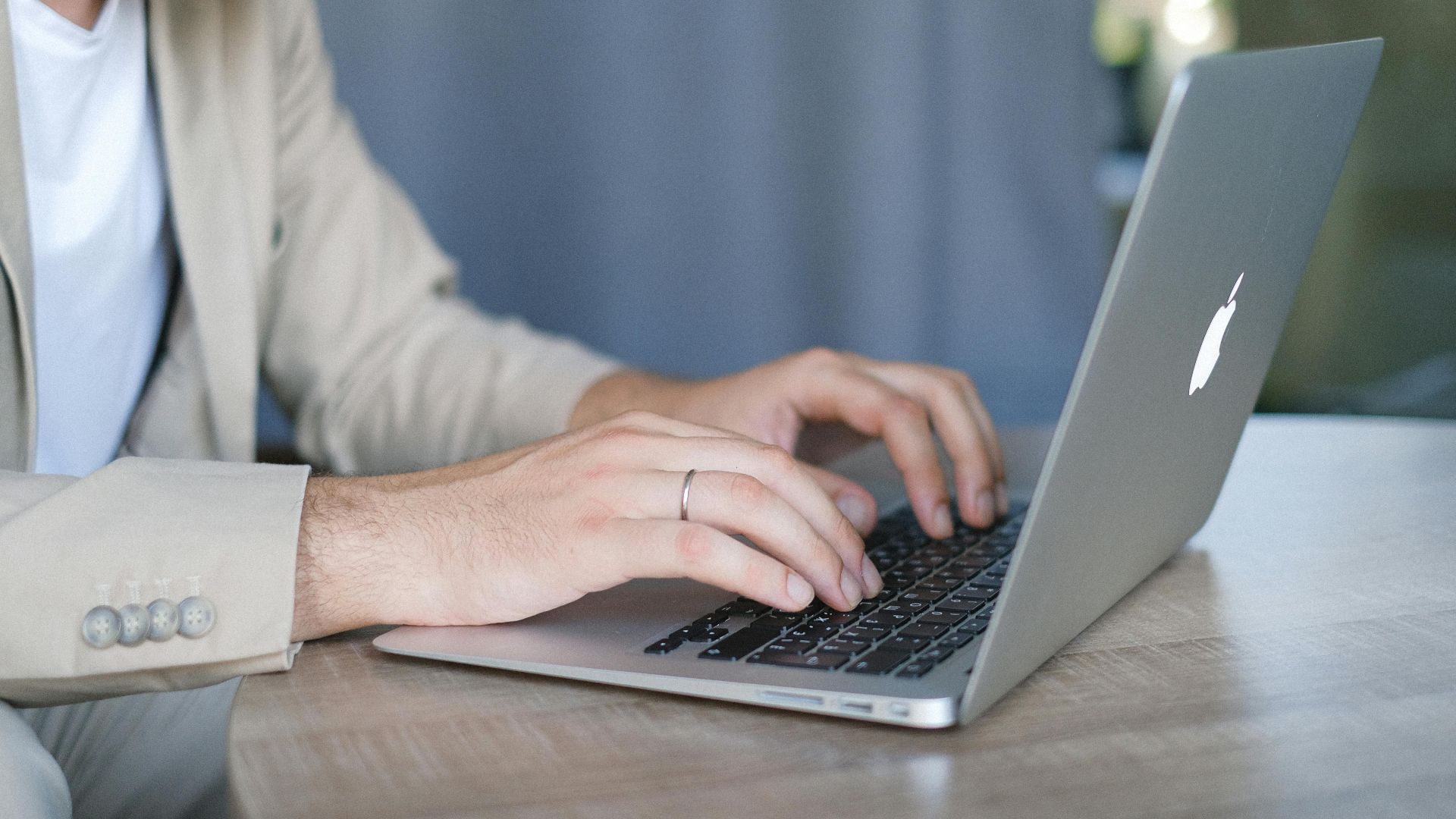 Side view of crop bearded male entrepreneur wearing classy jacket sitting at wooden table and browsing modern netbook in daylight
