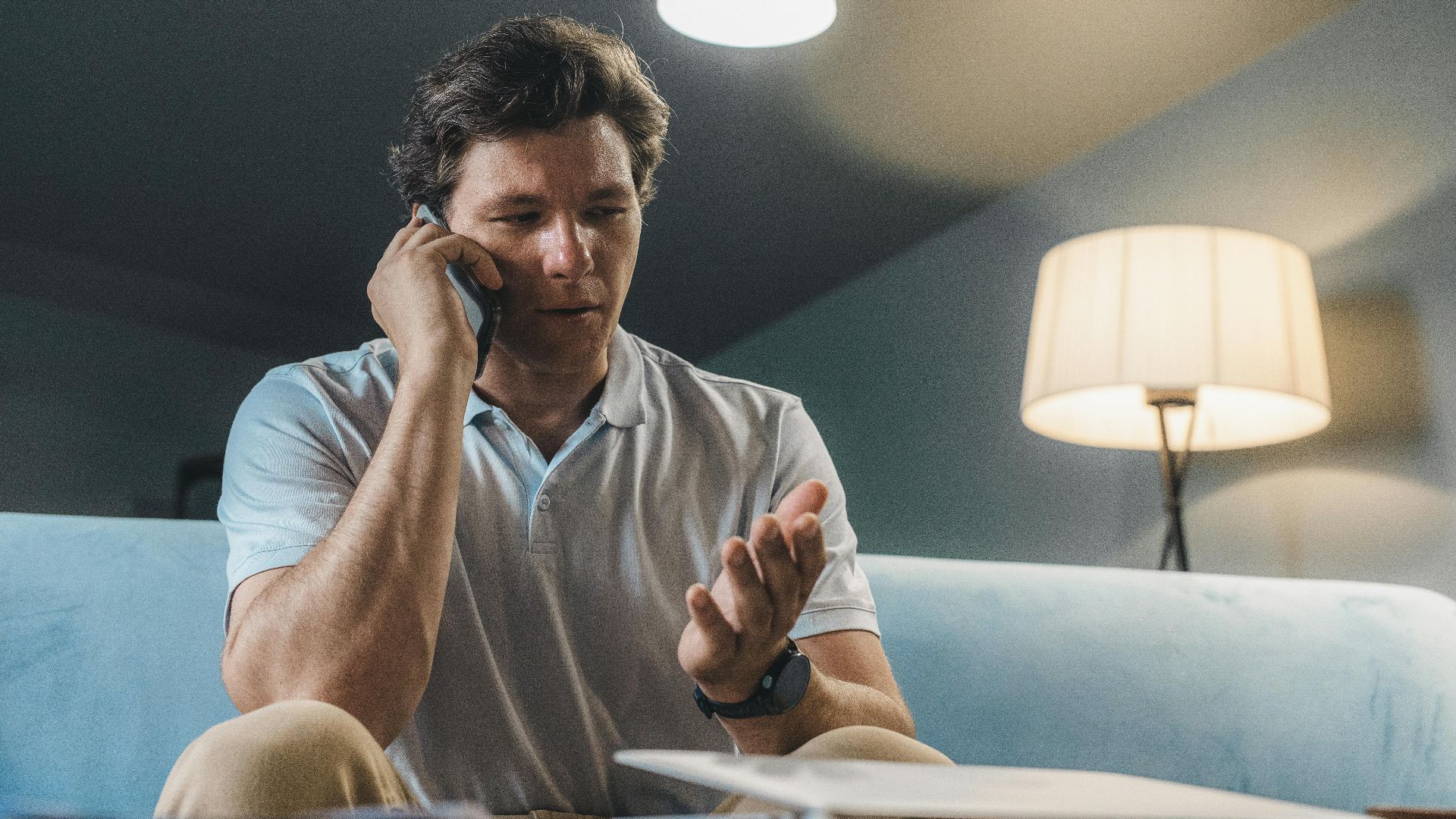 Man speaking on a smartphone while sitting on a sofa, working from home.