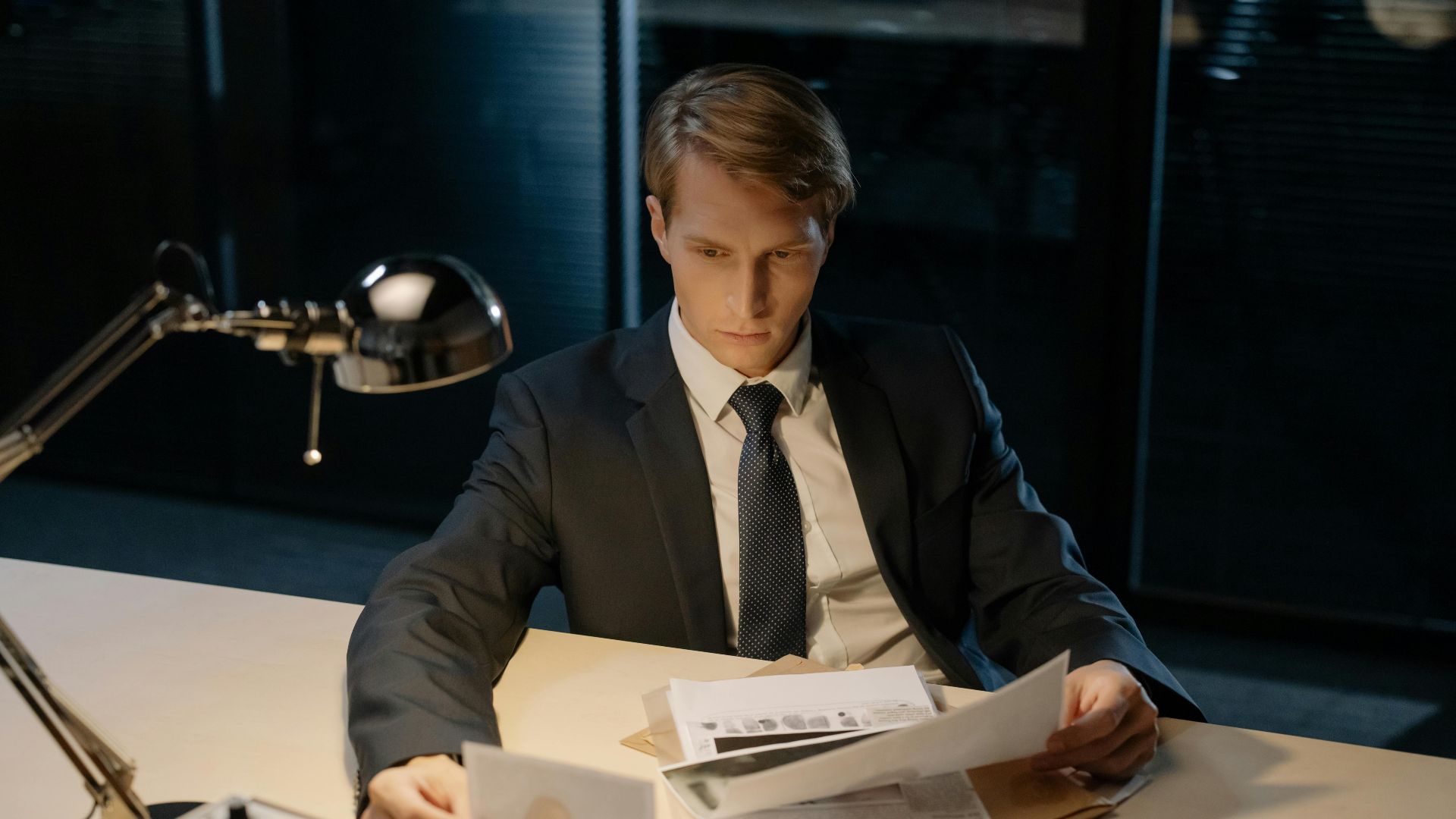 Focused investigator reviewing evidence in a dimly lit office setting.