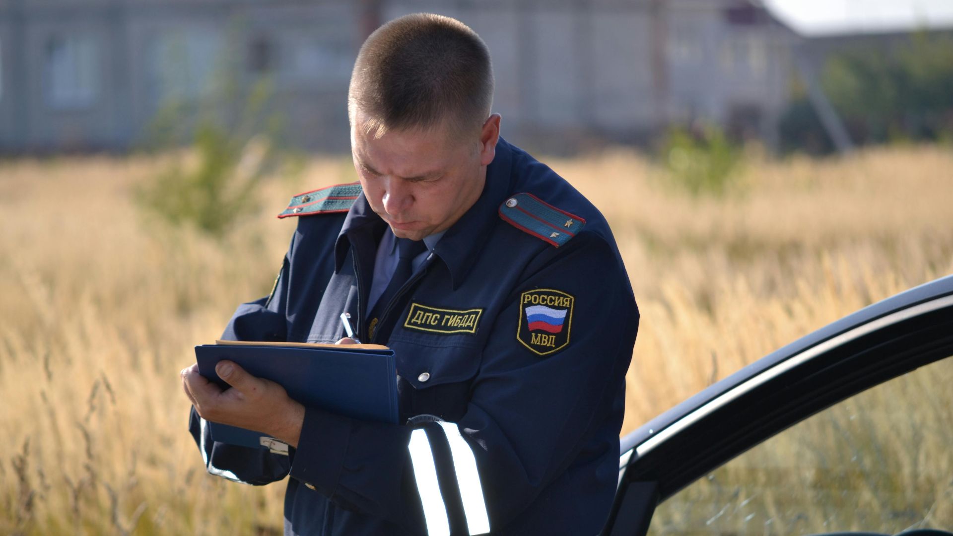 Police officer in uniform taking notes beside a car in a field.