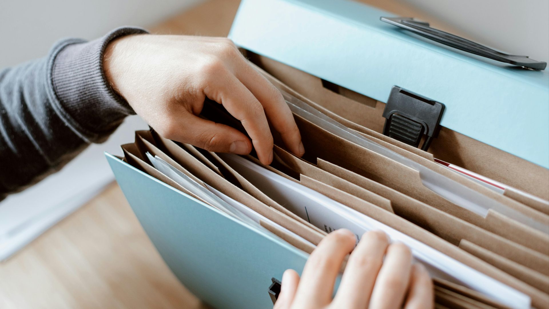 Crop unrecognizable person selecting document in opened briefcase for documents placed on wooden table