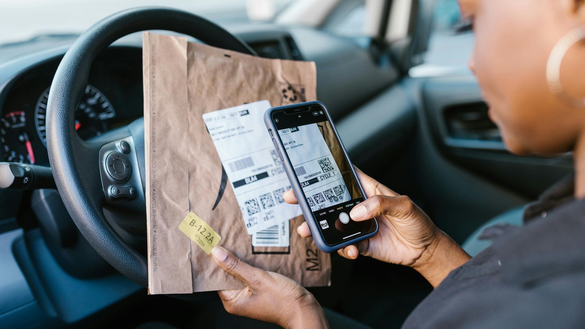 Close-up of a courier in a car scanning a package label with a smartphone for delivery service.