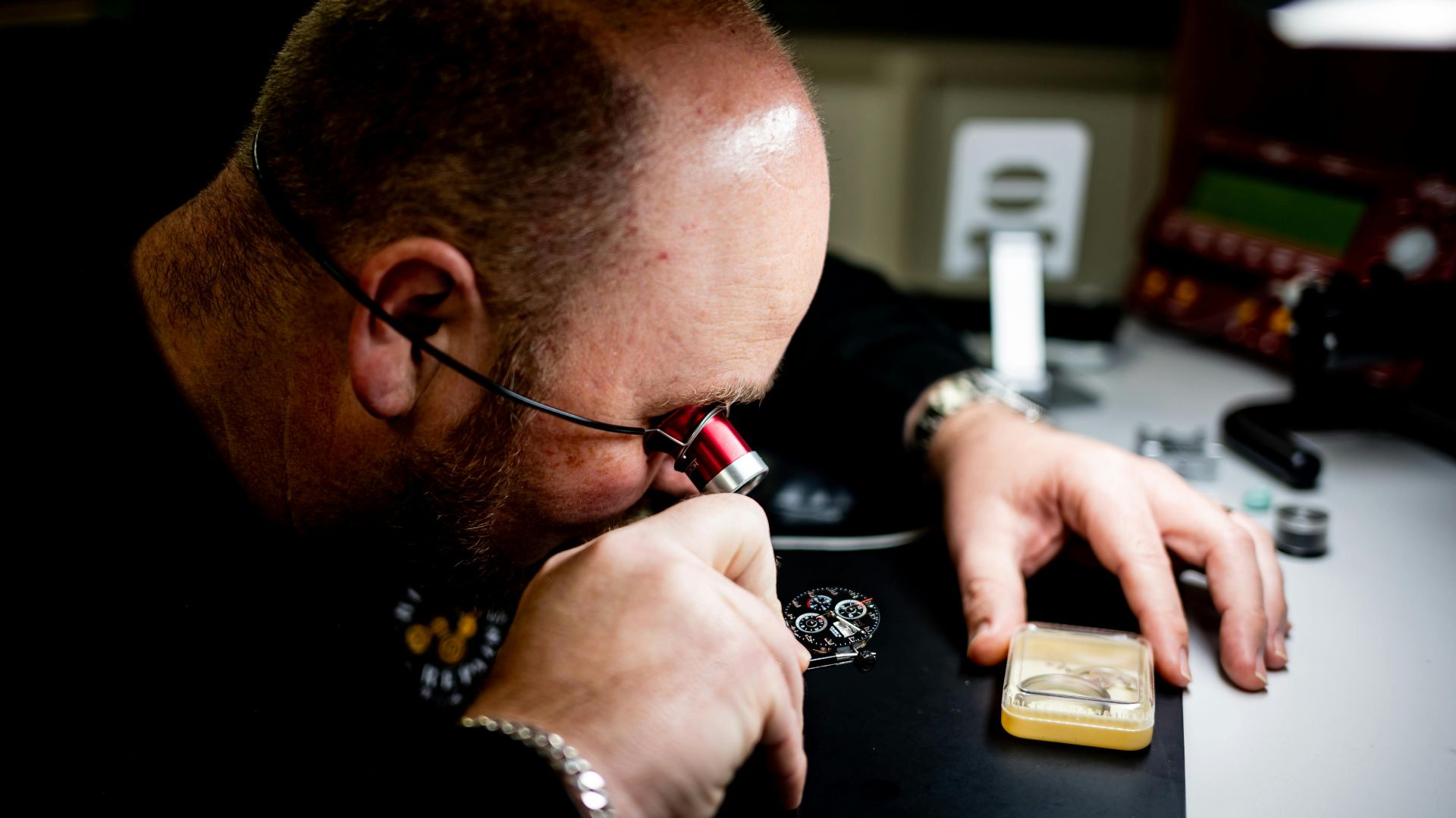 Skilled artisan closely inspects a watch mechanism using magnifying glass for precision