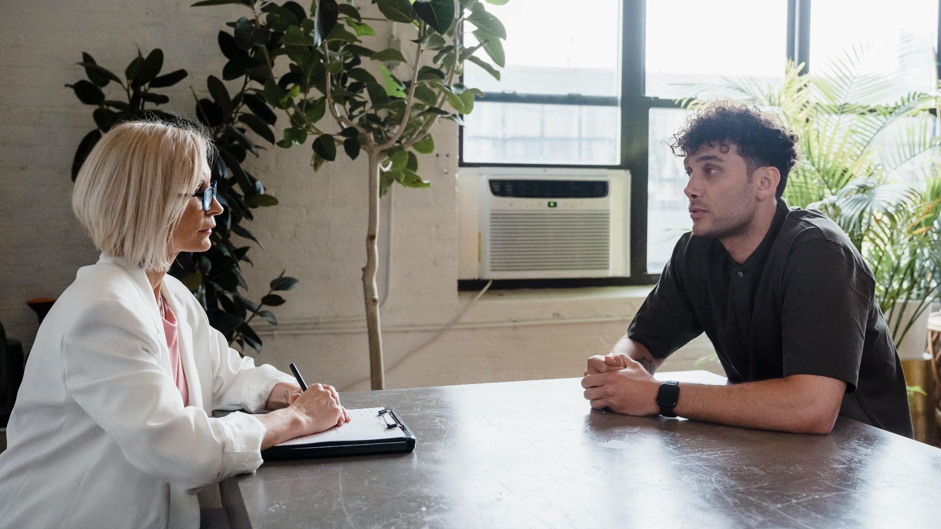 Two professionals engaged in a discussion in a modern office with natural light and plants.
