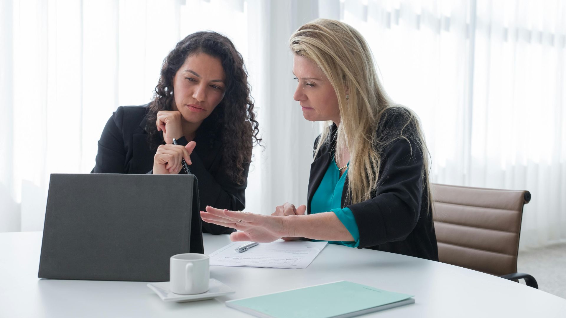 Two businesswomen in a focused discussion at a modern office desk.