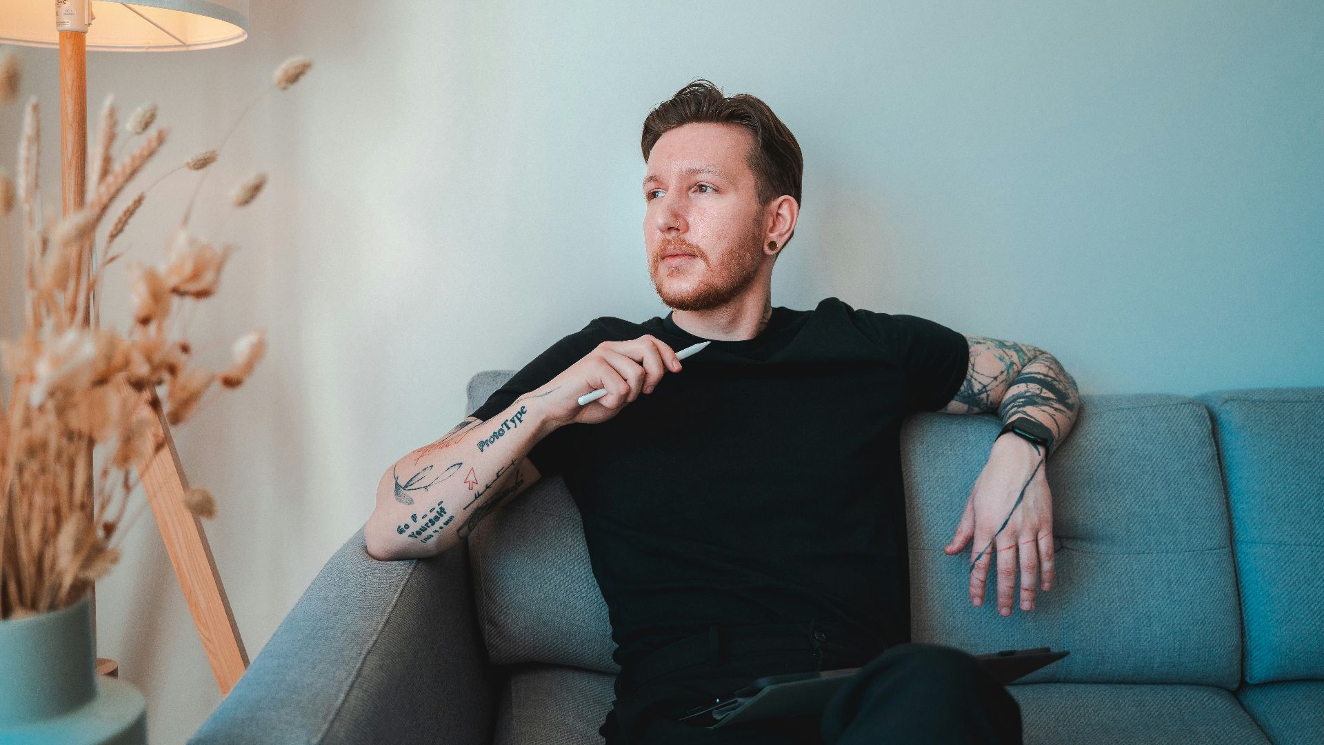 a man sitting on a couch with tattoos on his arm