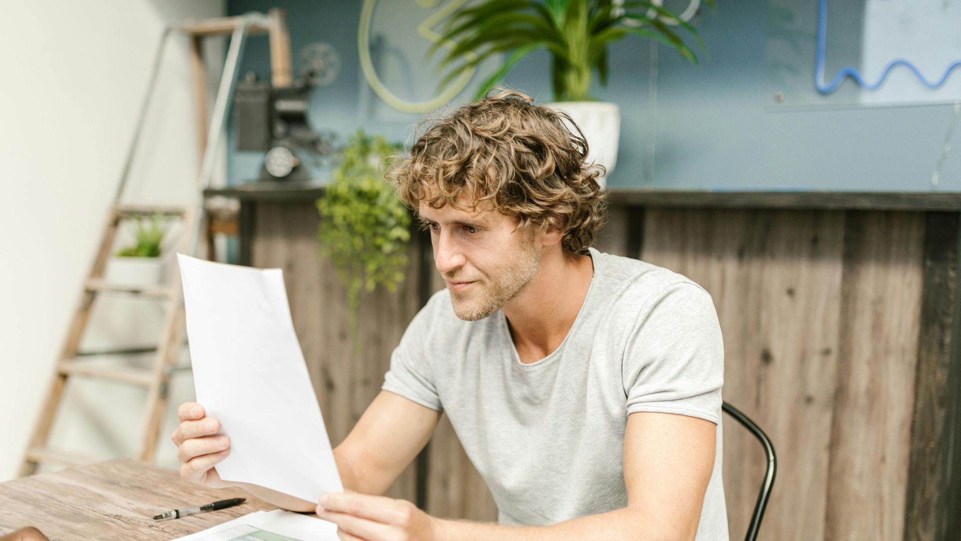 A man with curly hair evaluates documents at a desk, highlighting focused work in a professional setting.