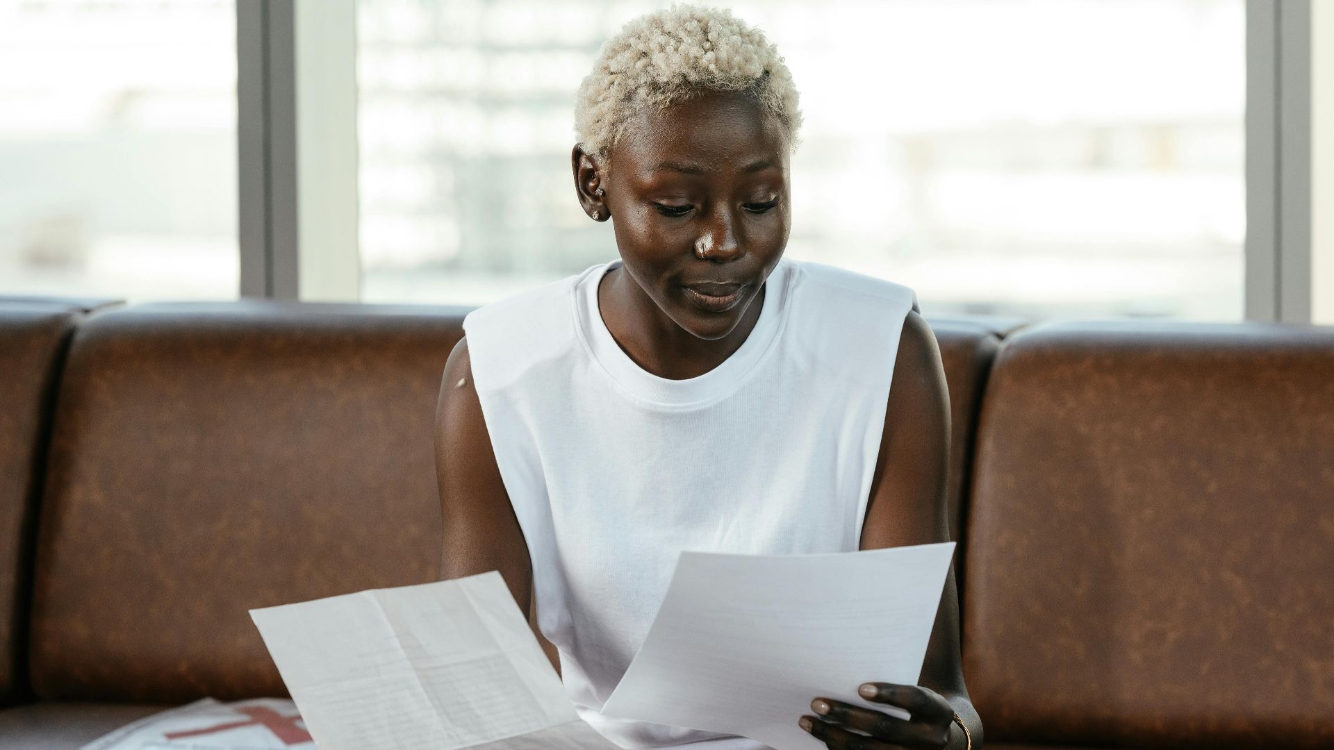 Concentrated African American female comparing important papers of report on leather sofa in office