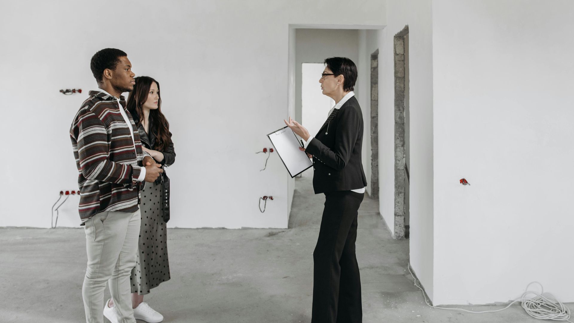 Real estate agent showing a house to a couple in a newly built home interior.