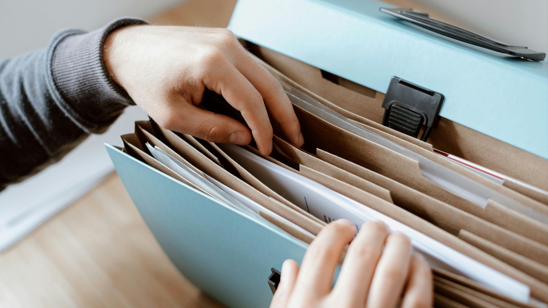 Crop unrecognizable person selecting document in opened briefcase for documents placed on wooden table