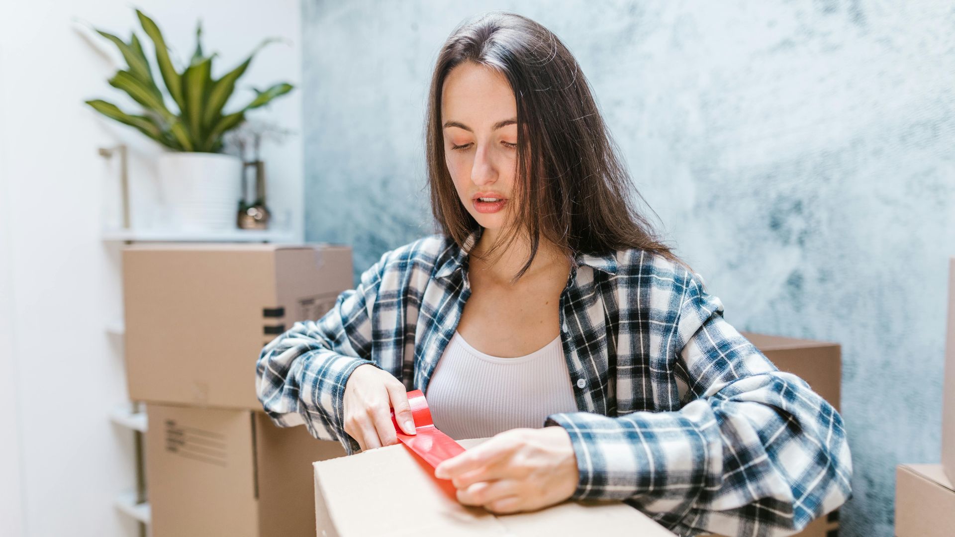 Woman sealing boxes with tape for relocation in a cozy indoor setting.