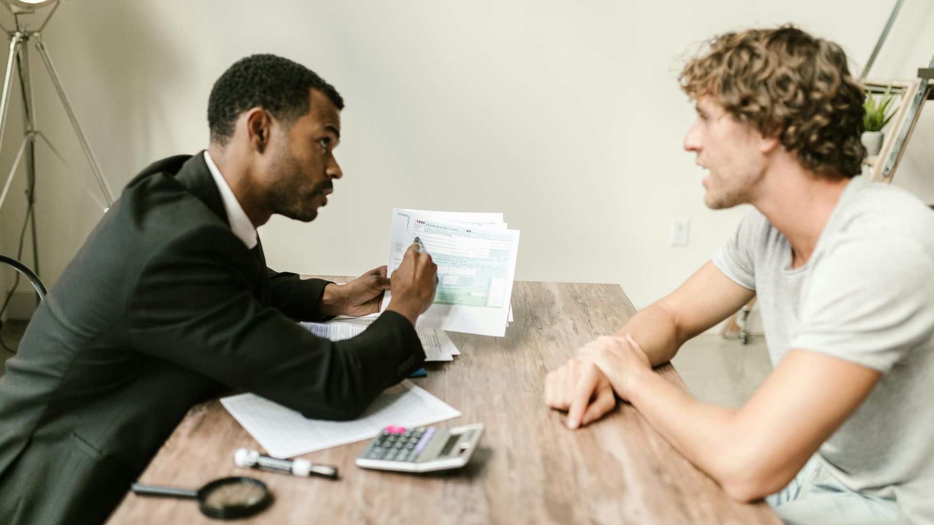 A financial advisor discusses paperwork with a client at a desk in a modern office.