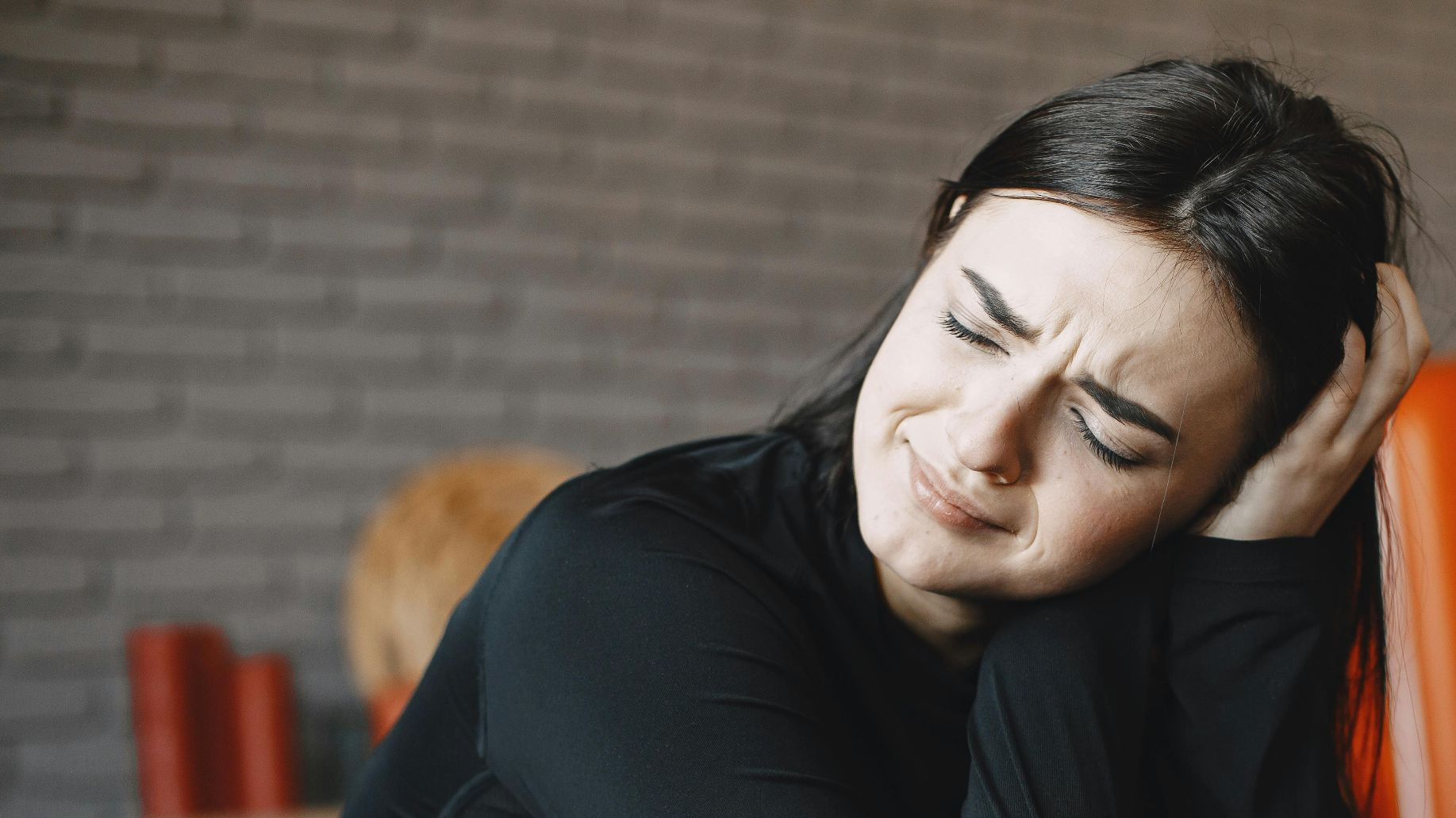 A woman displays emotional distress while sitting indoors, conveying feelings of anxiety and worry.