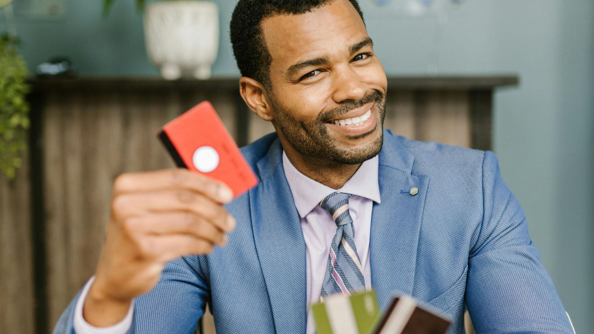 Smiling man in suit holding credit cards at a desk indoors, showcasing financial confidence.