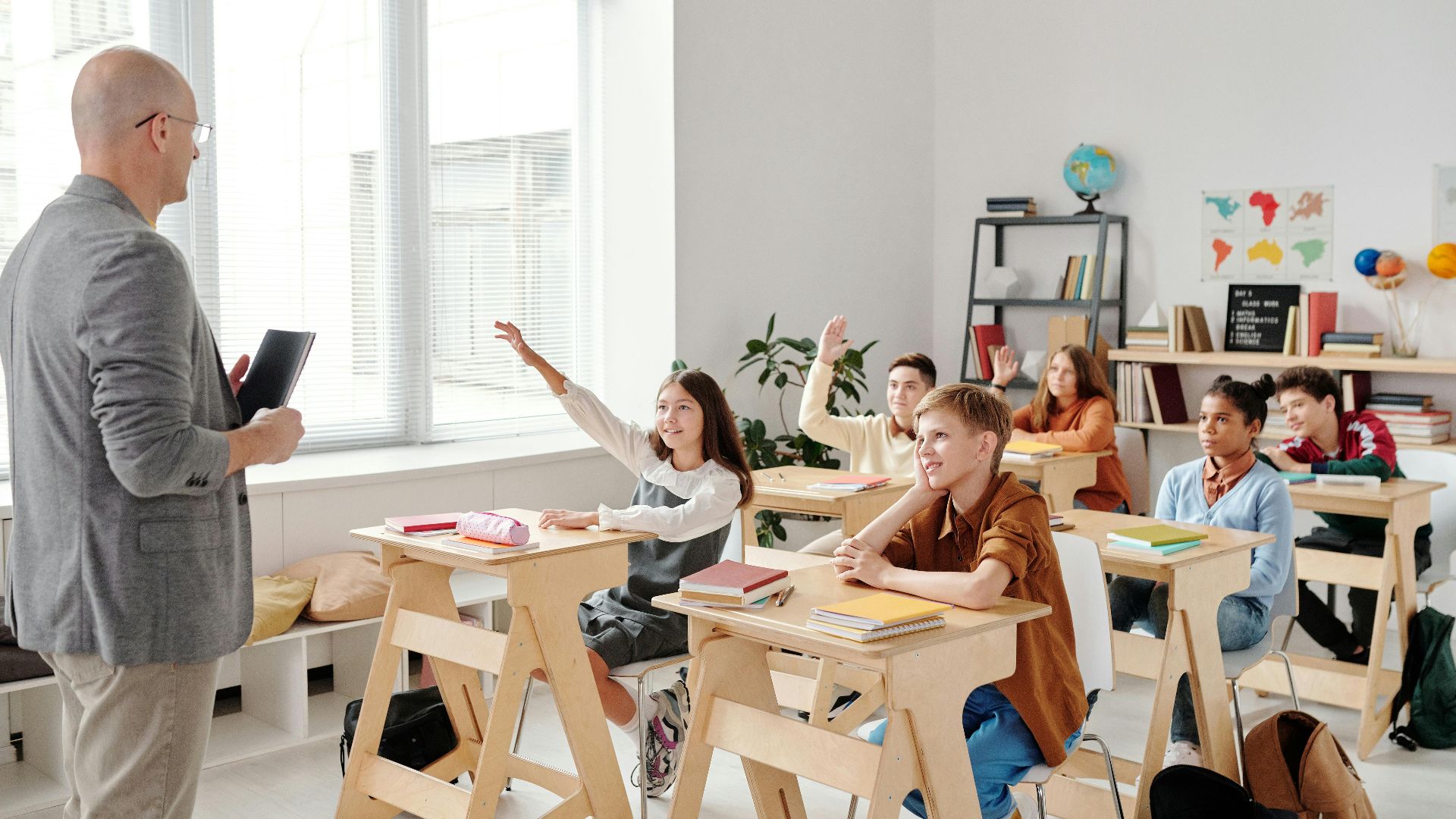 Students engage eagerly in a classroom, raising hands and participating in a lesson with their teacher.