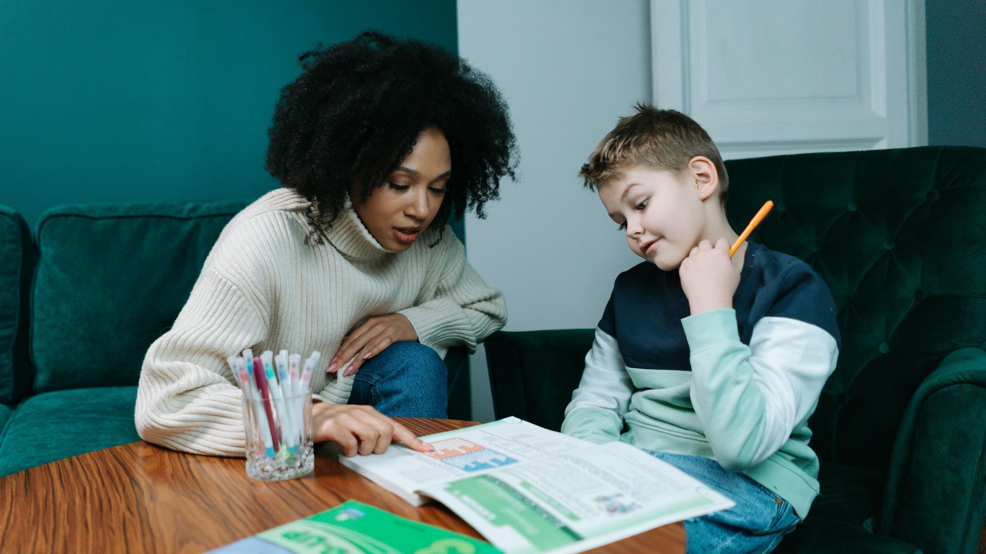 Woman guiding child in studying at home with books on a cozy couch.
