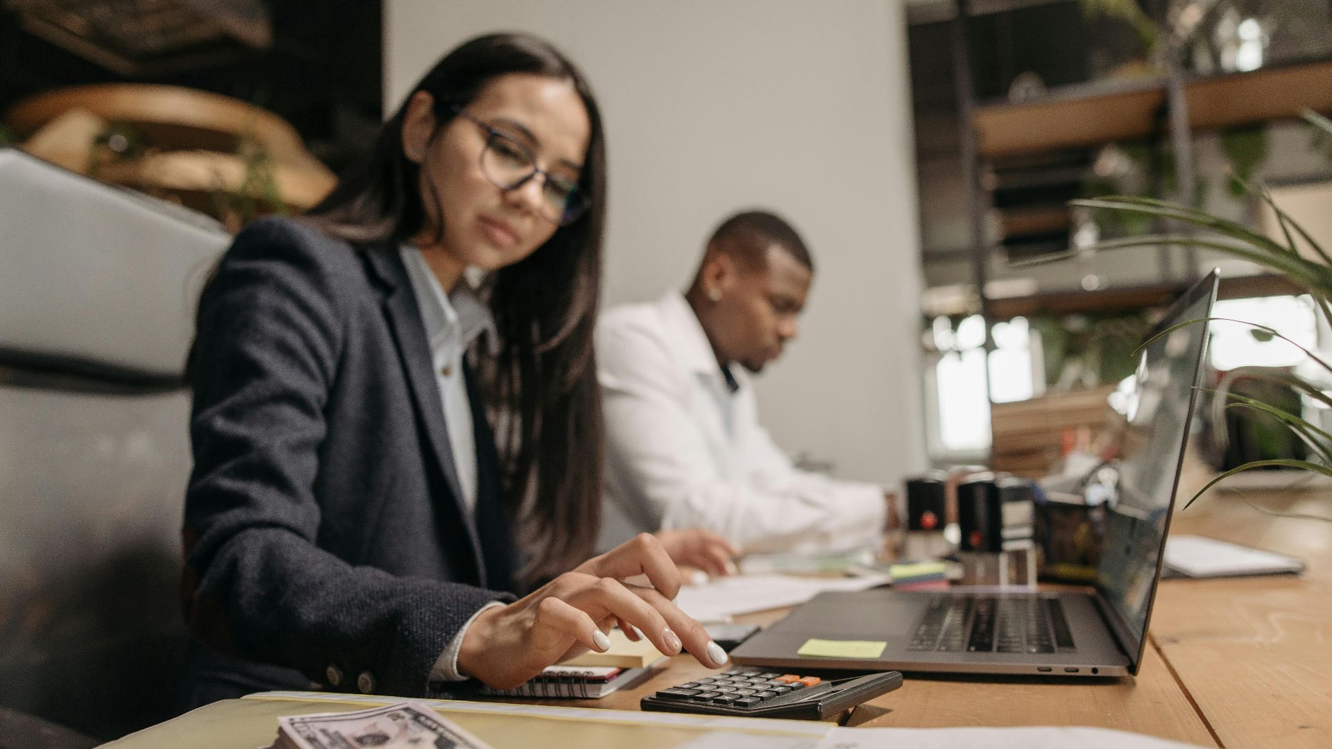 Two business professionals collaborating with a laptop and calculator in a modern office.