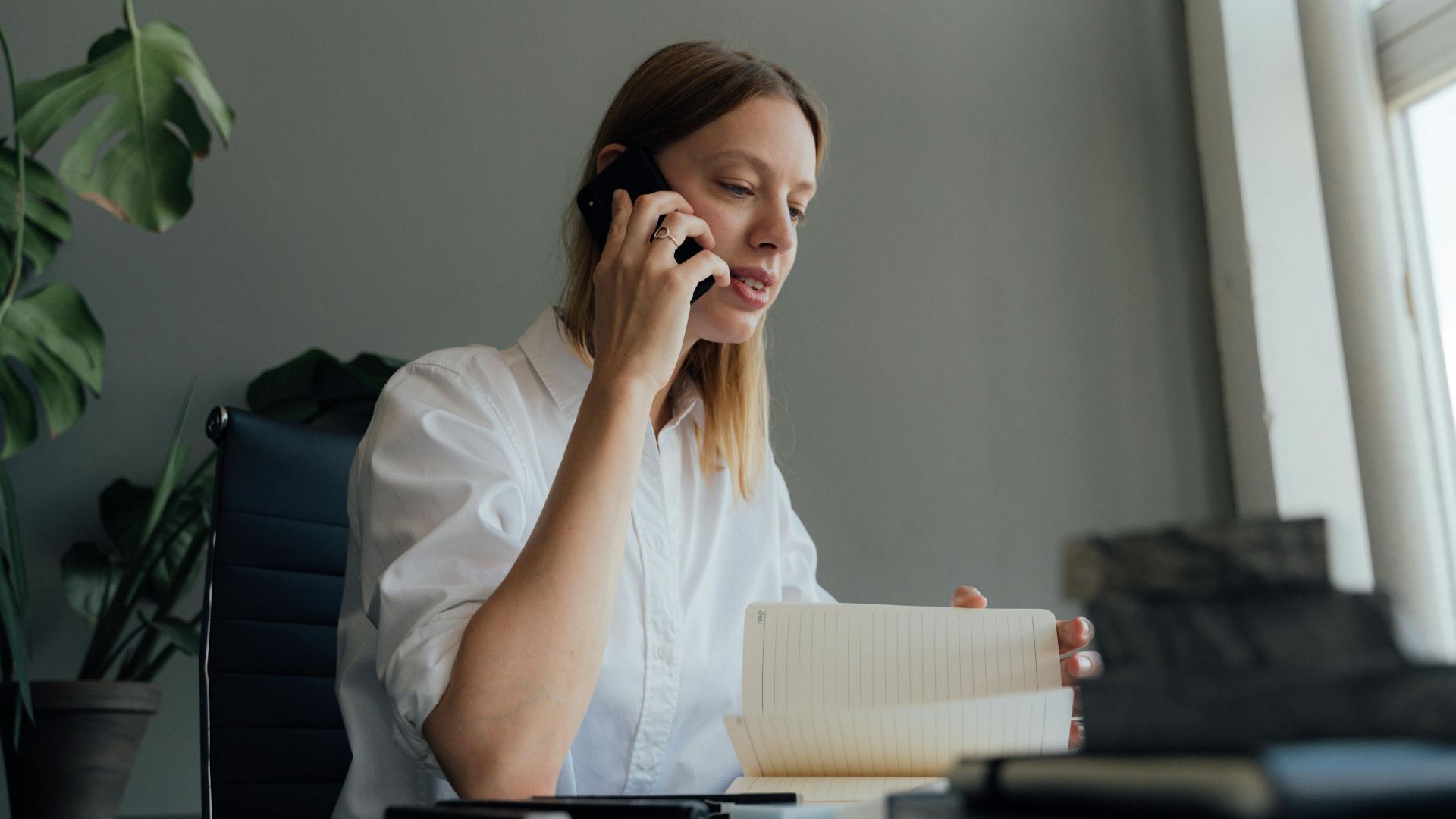 Woman on a phone call while reviewing documents at her desk indoors.