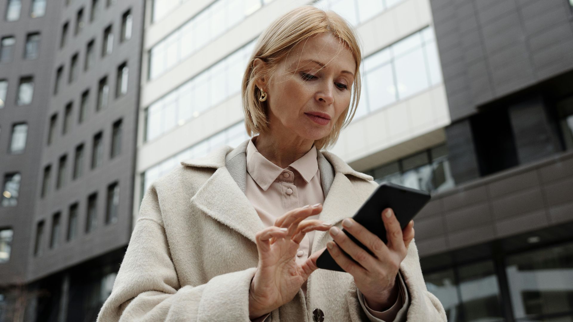 Woman in coat using smartphone in front of modern building. Professional and focused expression.