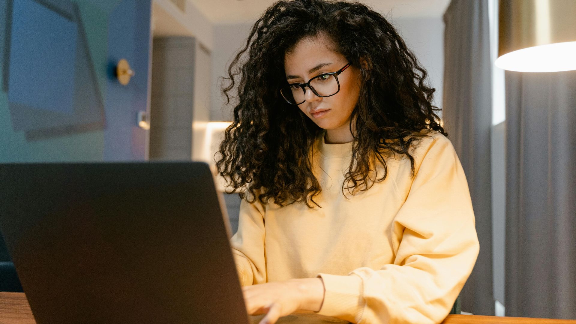 Woman in yellow sweater working on a laptop in a cozy home setting.