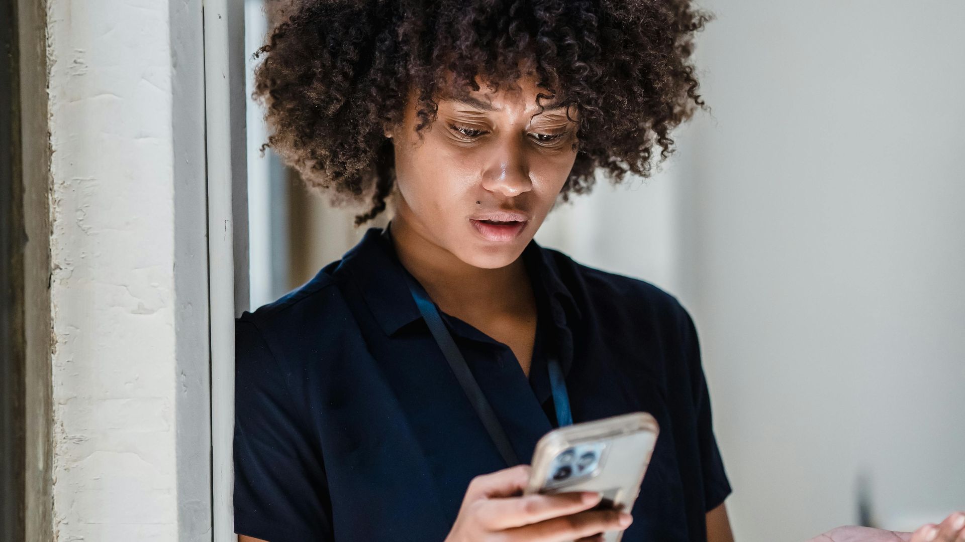 A woman with curly hair gesturing emotionally while engaged in a phone call indoors.