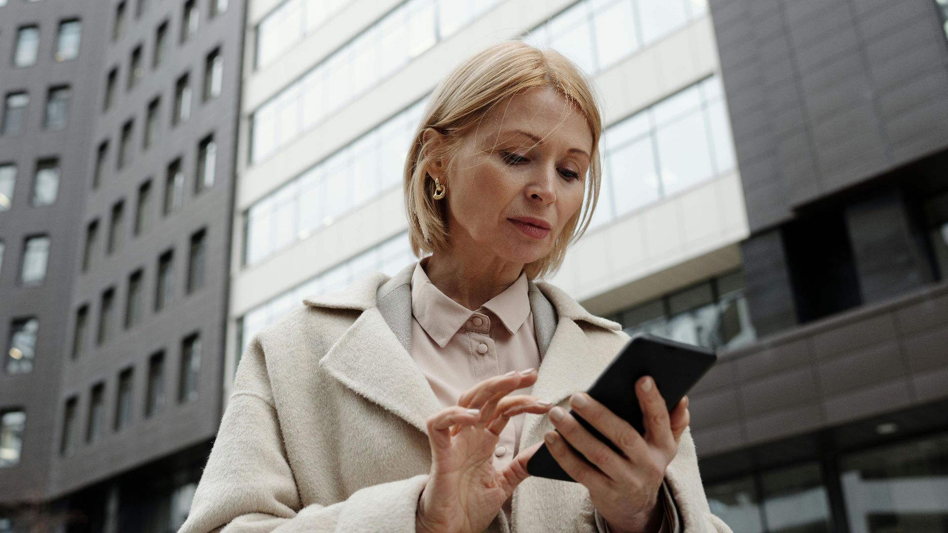 Woman in coat using smartphone in front of modern building. Professional and focused expression.