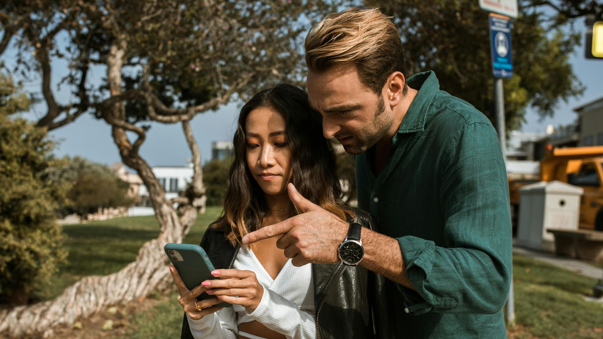 A man and woman using a smartphone together in a city park during daytime.