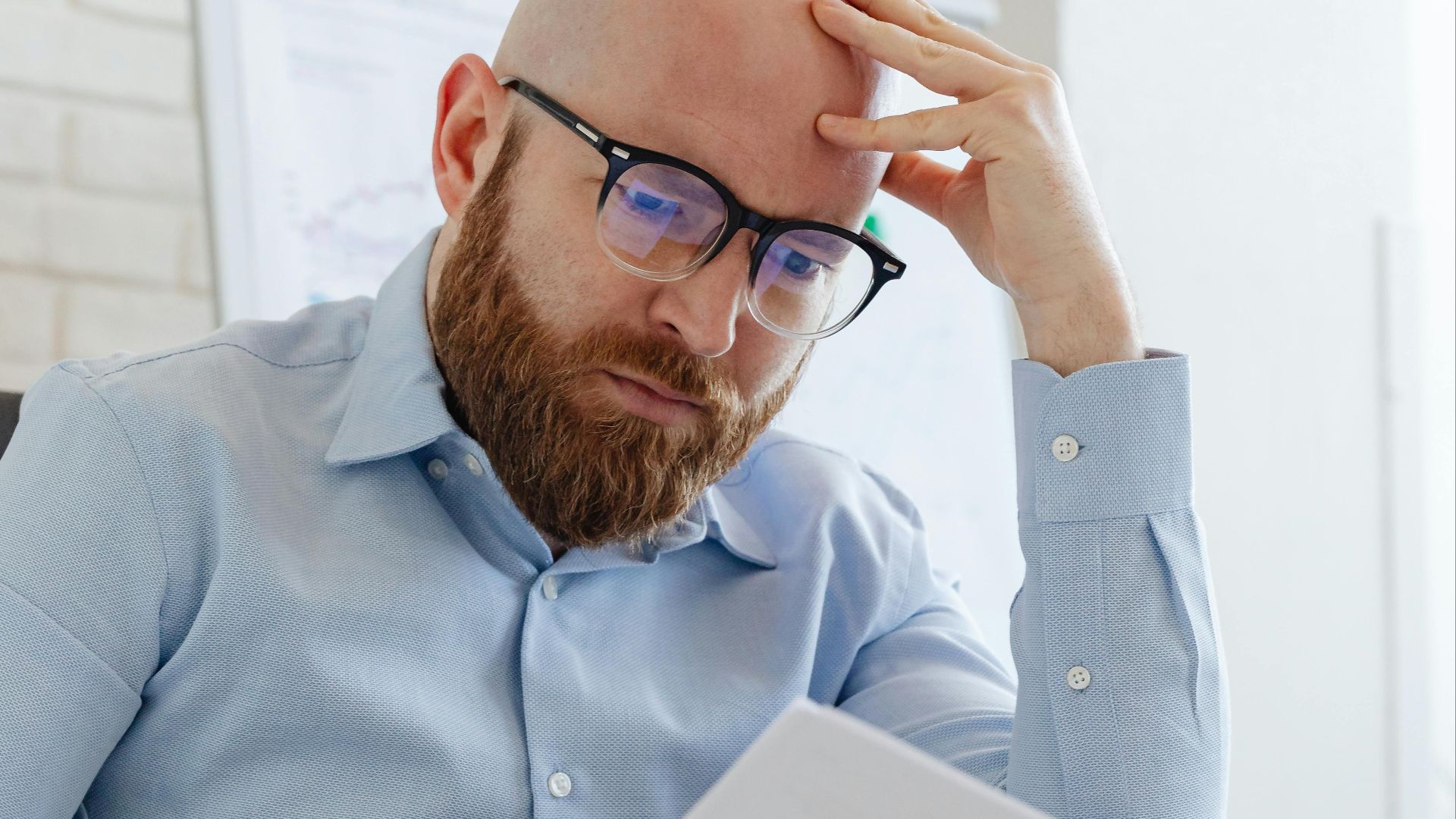 Caucasian businessman with beard and glasses reviewing documents in a modern office setting.