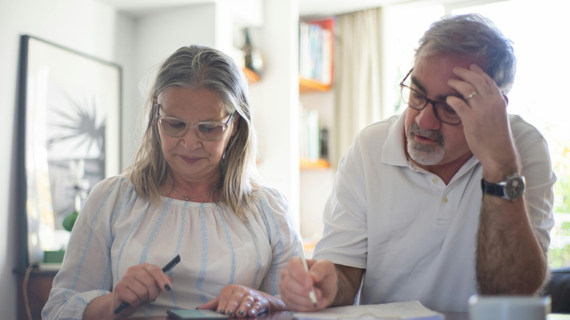 Senior couple calculating expenses at home office desk with documents and notes.