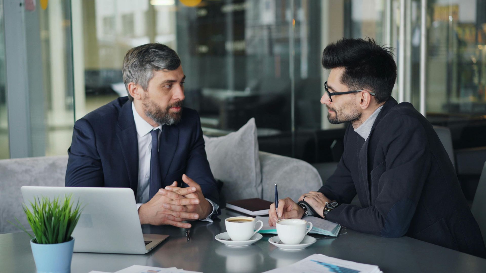 Two businessmen having a meeting with laptops, papers, and coffee at a modern office.