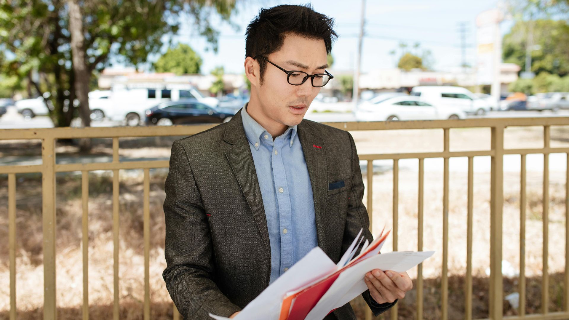 Asian businessman in a suit checking documents outdoors on a sunny day.