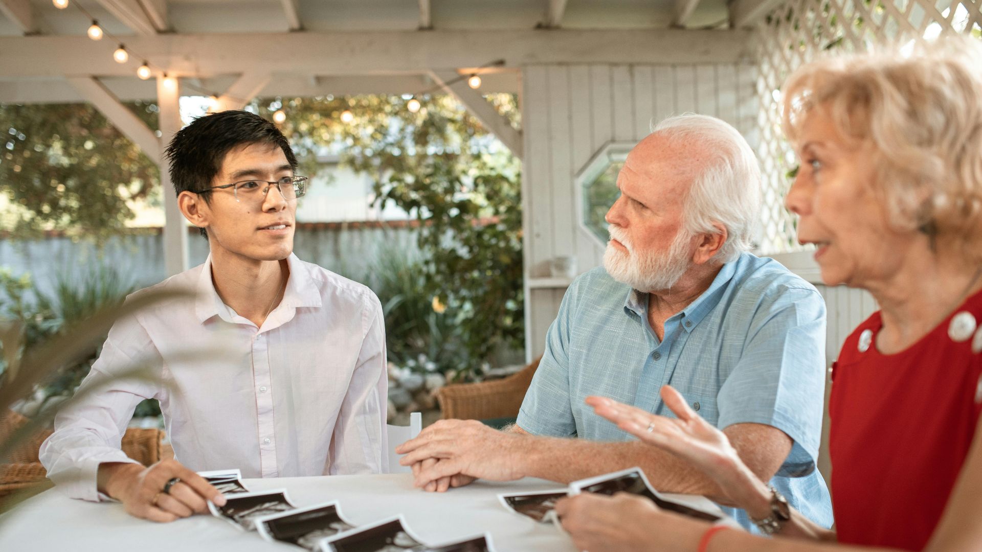 Senior couple and family member discussing ultrasound photos at an outdoor table.