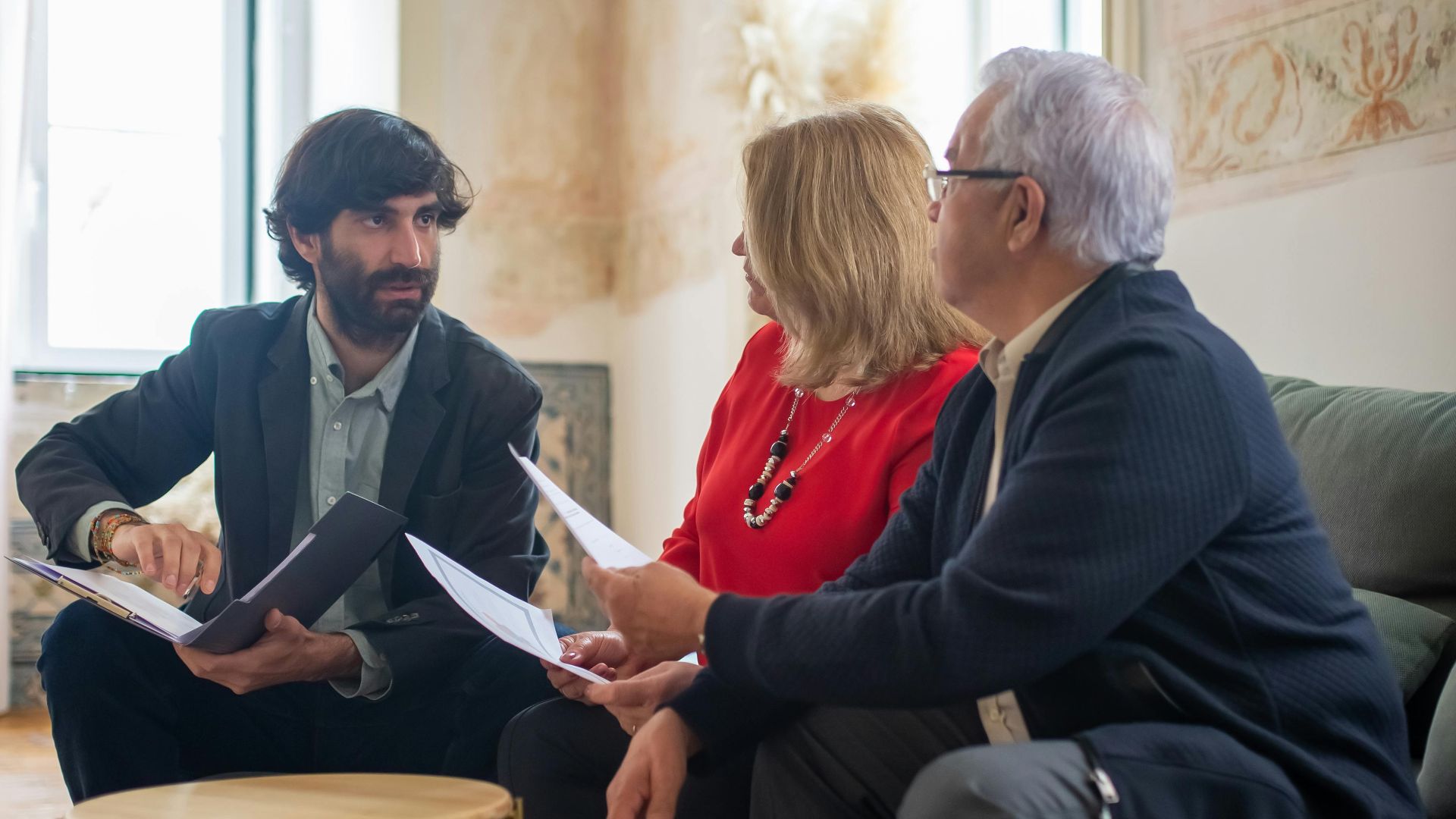 An advisor discussing financial documents with a senior couple indoors in a cozy living room setting.