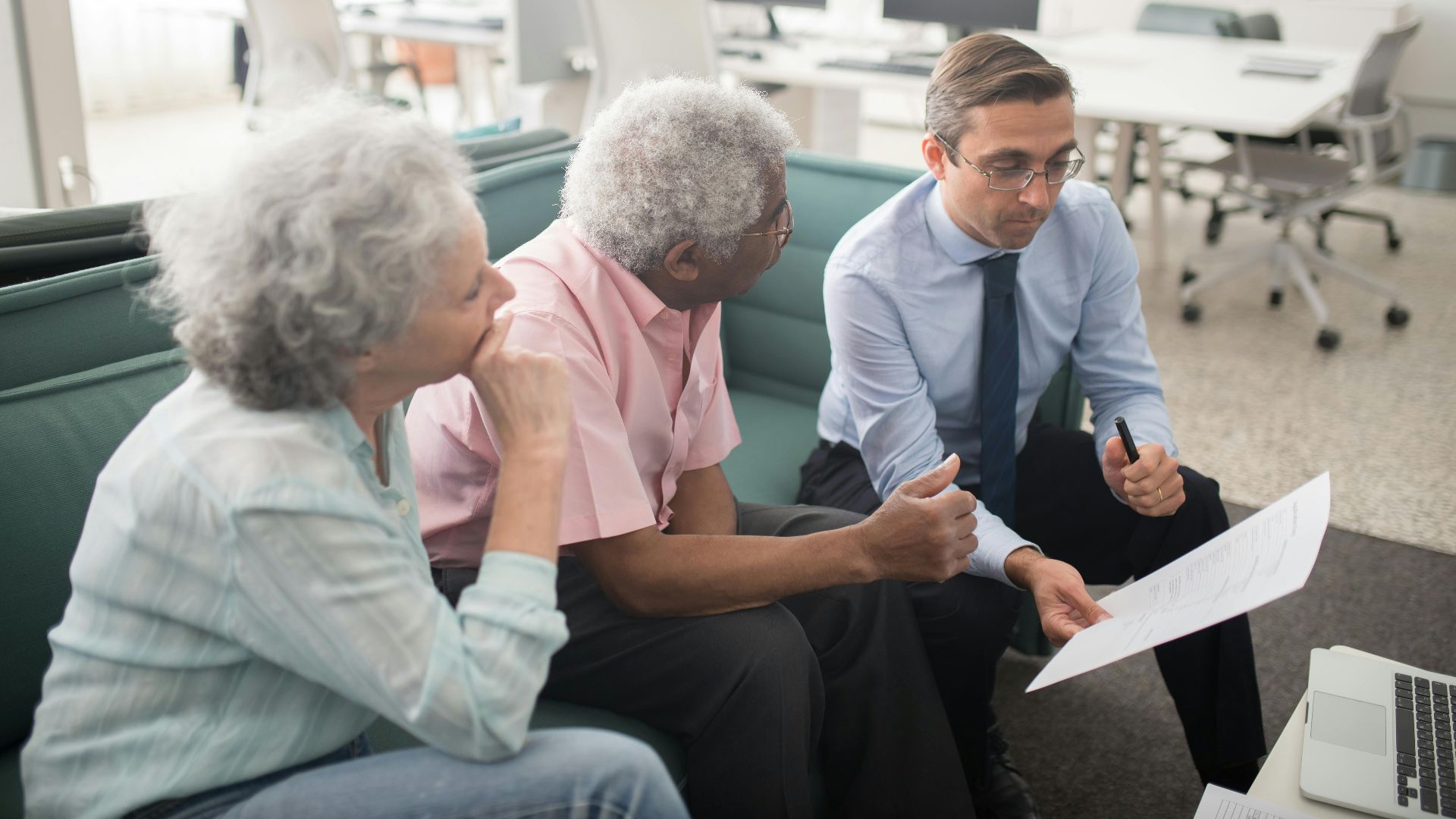 Business professional consults elderly clients in an office setting. Collaborative discussion, paperwork visible.