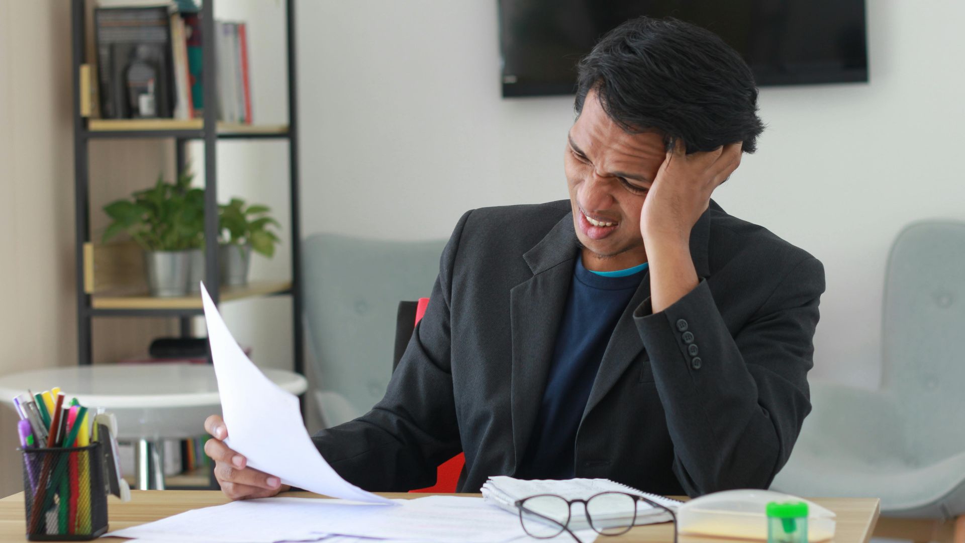 A businessman in an office experiencing stress while reviewing documents.