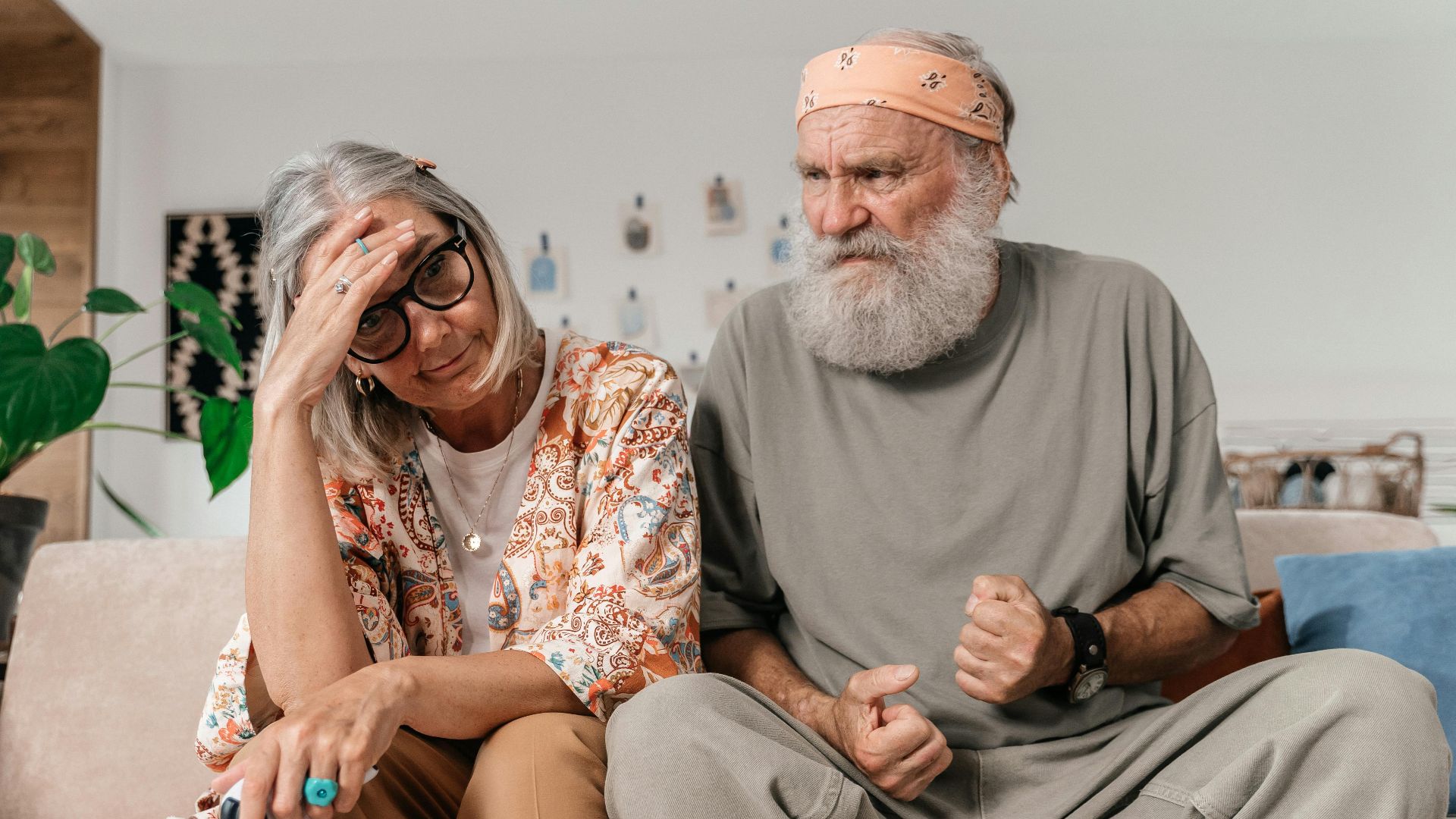 Senior couple expressing frustration while sitting on sofa indoors.